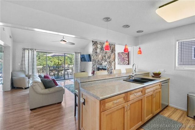 kitchen featuring a stone fireplace, pendant lighting, sink, stainless steel dishwasher, and light hardwood / wood-style floors