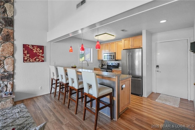 kitchen with light hardwood / wood-style flooring, stainless steel appliances, a kitchen breakfast bar, decorative light fixtures, and kitchen peninsula