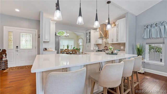 kitchen featuring decorative light fixtures, white cabinetry, a kitchen breakfast bar, a large island, and wall chimney range hood