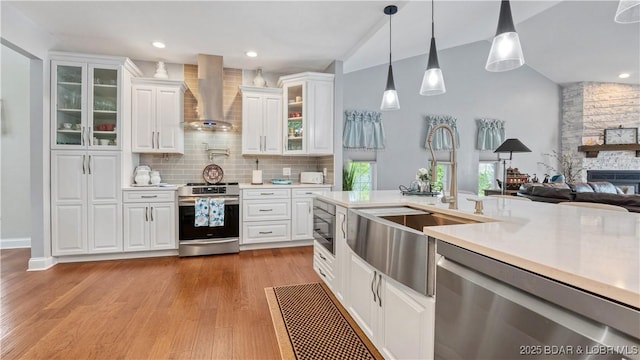 kitchen featuring pendant lighting, wall chimney range hood, sink, appliances with stainless steel finishes, and white cabinetry