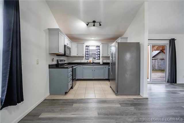 kitchen with gray cabinets, vaulted ceiling, sink, light hardwood / wood-style floors, and stainless steel appliances