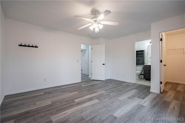 unfurnished bedroom featuring a spacious closet, wood-type flooring, ceiling fan, and ensuite bathroom