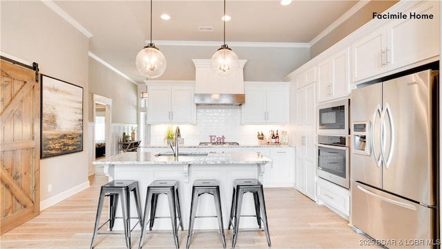 kitchen with light stone counters, an island with sink, pendant lighting, stainless steel appliances, and white cabinets