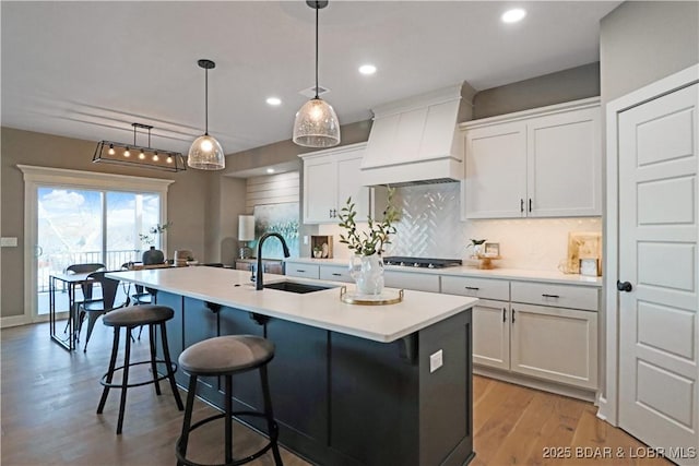 kitchen with premium range hood, white cabinetry, an island with sink, and sink