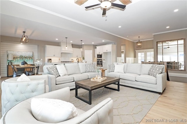 living room with sink, crown molding, light hardwood / wood-style floors, and ceiling fan