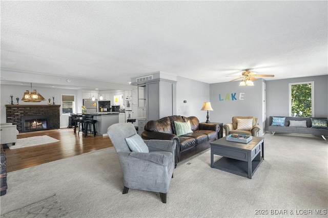 carpeted living room with ceiling fan, a textured ceiling, and a fireplace