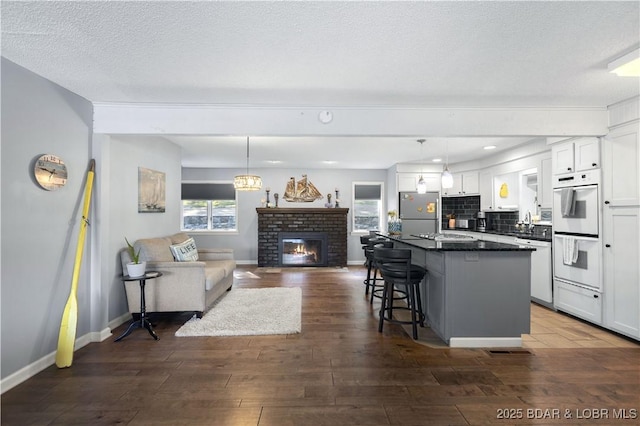 kitchen featuring stainless steel fridge, white cabinetry, hanging light fixtures, a center island, and a brick fireplace