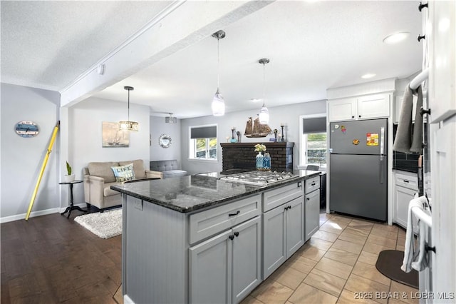 kitchen featuring hanging light fixtures, appliances with stainless steel finishes, gray cabinets, a kitchen island, and dark stone counters