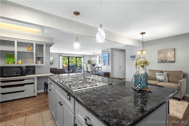 kitchen featuring pendant lighting, dark stone countertops, a notable chandelier, a kitchen island, and stainless steel gas stovetop