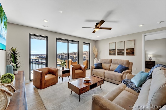 living room with light hardwood / wood-style flooring, ceiling fan, and a water view