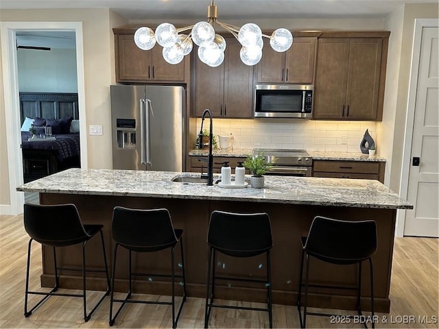 kitchen featuring light wood-type flooring, a center island with sink, light stone countertops, and appliances with stainless steel finishes