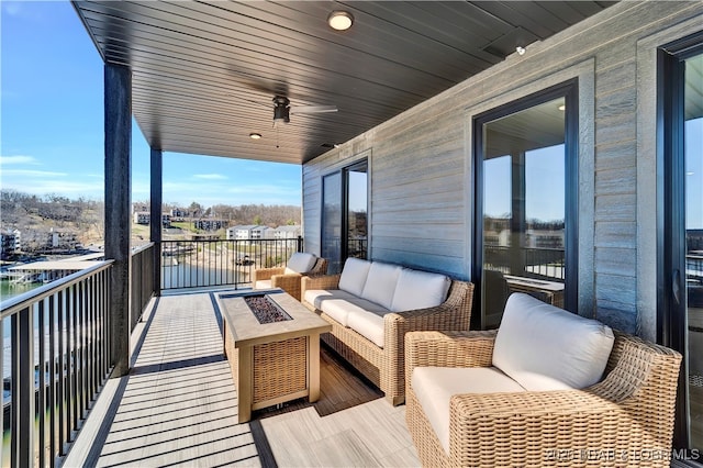 balcony with a water view, ceiling fan, and an outdoor living space with a fire pit