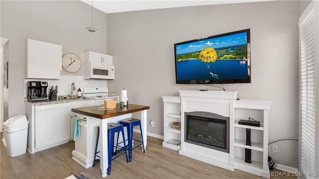 kitchen featuring white appliances, a sink, white cabinets, light wood-type flooring, and backsplash