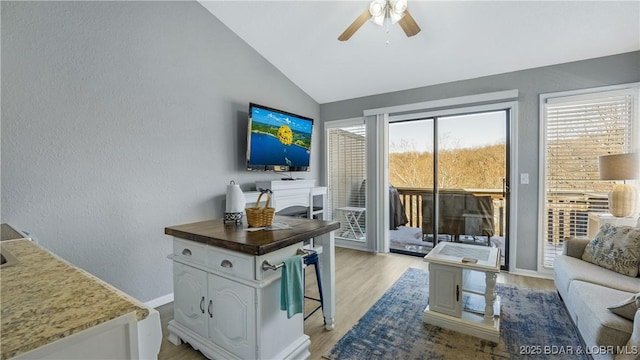 living room featuring a ceiling fan, light wood-type flooring, vaulted ceiling, and baseboards