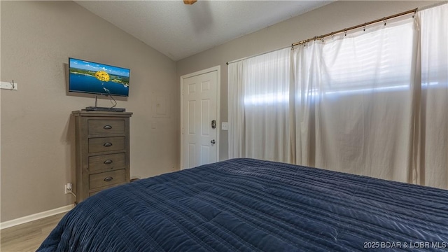 bedroom featuring lofted ceiling, baseboards, and wood finished floors