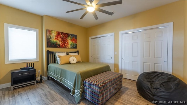 bedroom featuring hardwood / wood-style flooring, ceiling fan, and two closets