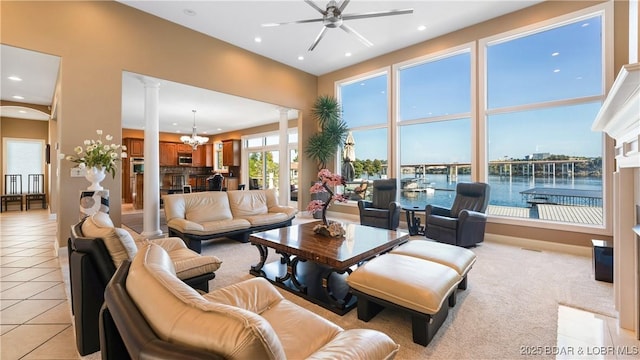 tiled living room with decorative columns, a water view, a high ceiling, and ceiling fan with notable chandelier