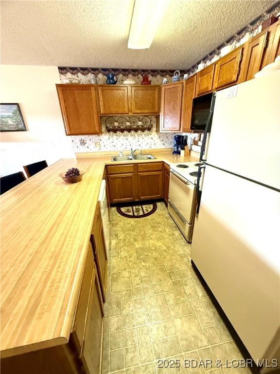 kitchen with butcher block counters, sink, a textured ceiling, and white appliances