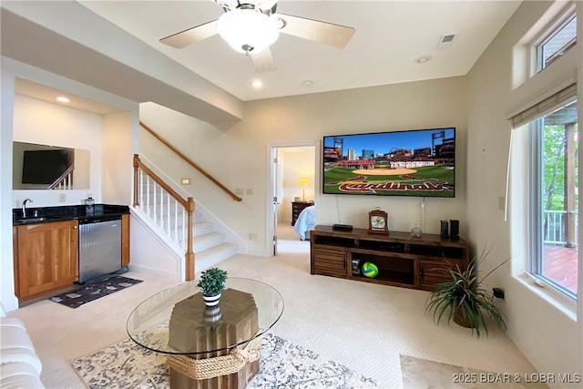 living room featuring wet bar, light colored carpet, and ceiling fan