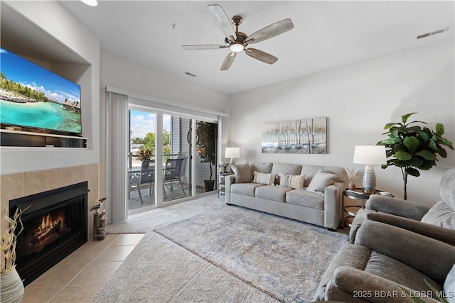 living room featuring ceiling fan, a tile fireplace, and light tile patterned floors