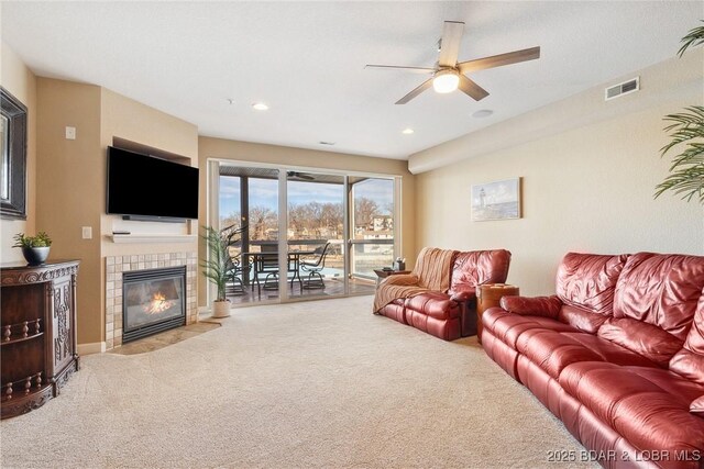 living room with a tile fireplace, ceiling fan, and carpet