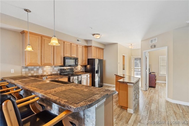 kitchen featuring a breakfast bar area, tasteful backsplash, decorative light fixtures, kitchen peninsula, and black appliances