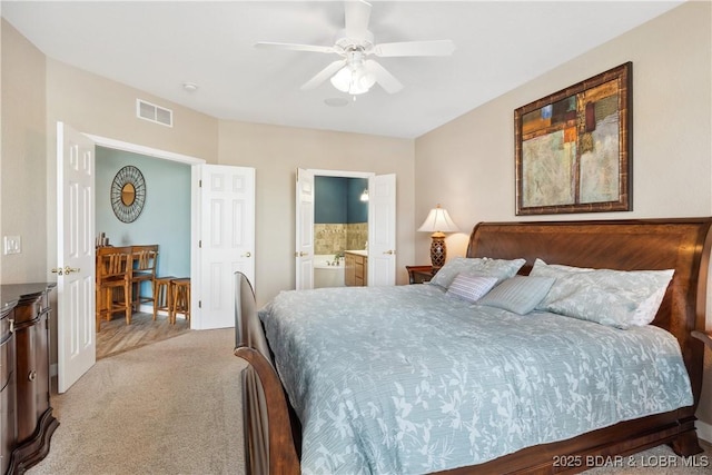 bedroom with ceiling fan, light colored carpet, and ensuite bath