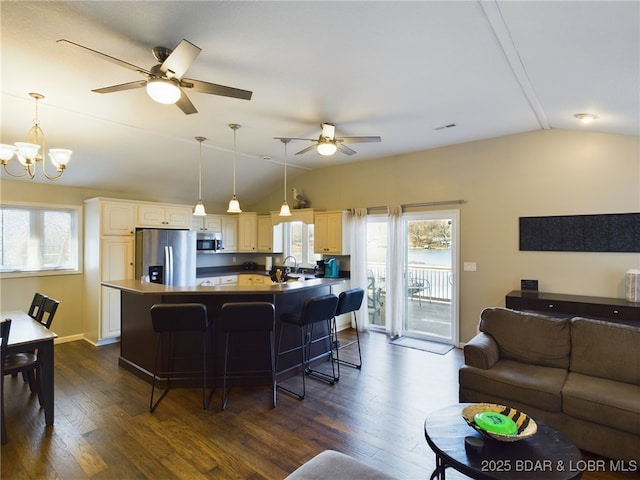 kitchen with vaulted ceiling, appliances with stainless steel finishes, dark hardwood / wood-style flooring, a kitchen breakfast bar, and a kitchen island with sink