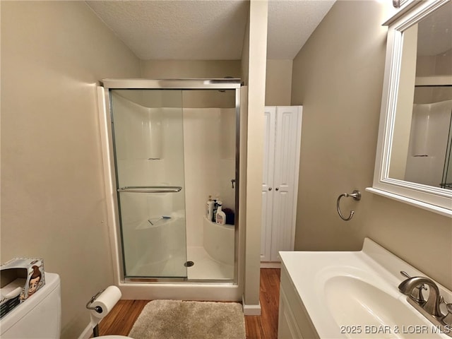 bathroom with toilet, a textured ceiling, vanity, a shower with door, and hardwood / wood-style flooring