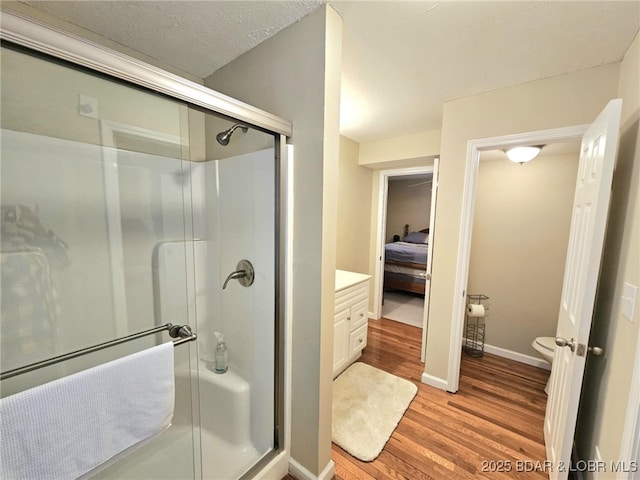 bathroom featuring hardwood / wood-style flooring, a shower with door, vanity, a textured ceiling, and toilet