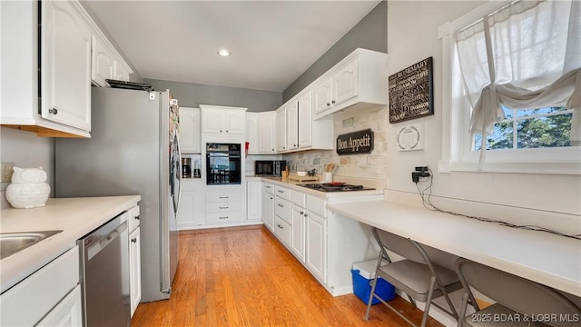 kitchen featuring built in desk, white cabinetry, backsplash, light hardwood / wood-style floors, and black appliances