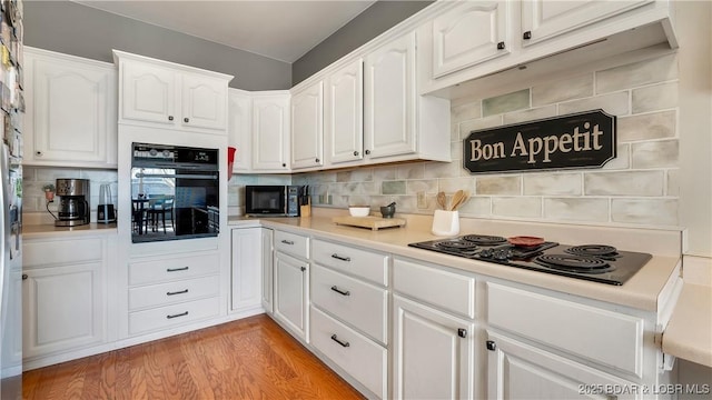 kitchen featuring white cabinets, light hardwood / wood-style floors, decorative backsplash, and black appliances