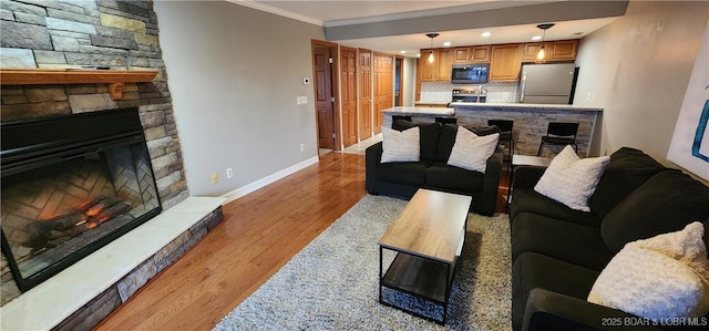 living room featuring crown molding, a stone fireplace, and light hardwood / wood-style floors