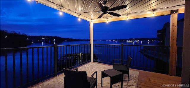 patio at twilight featuring a water view, ceiling fan, and a balcony