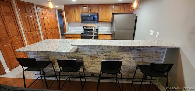 kitchen featuring a breakfast bar, stainless steel refrigerator, backsplash, light stone counters, and black / electric stove