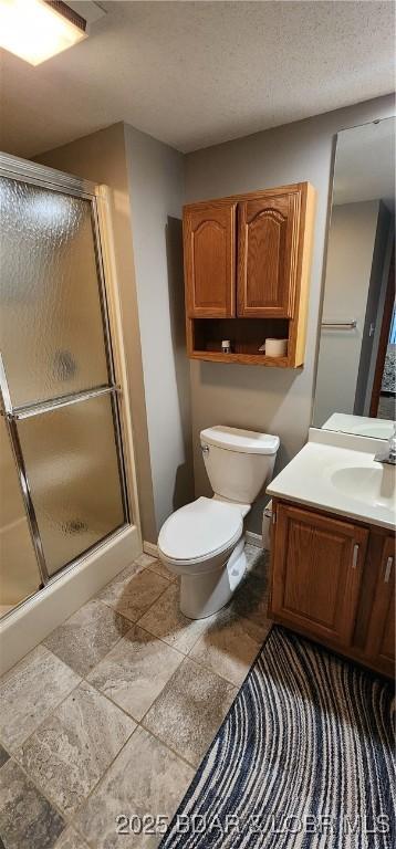 bathroom featuring vanity, toilet, a textured ceiling, and a shower with shower door