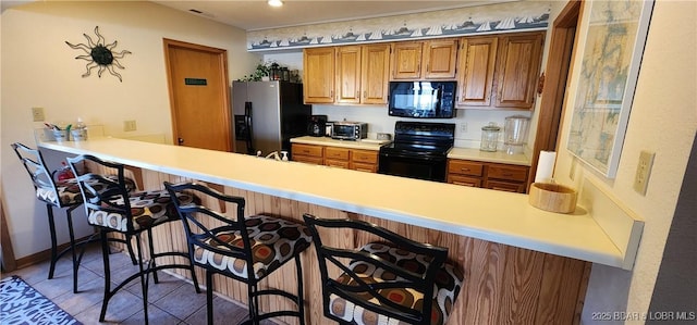 kitchen featuring kitchen peninsula, tile patterned flooring, a breakfast bar area, and black appliances