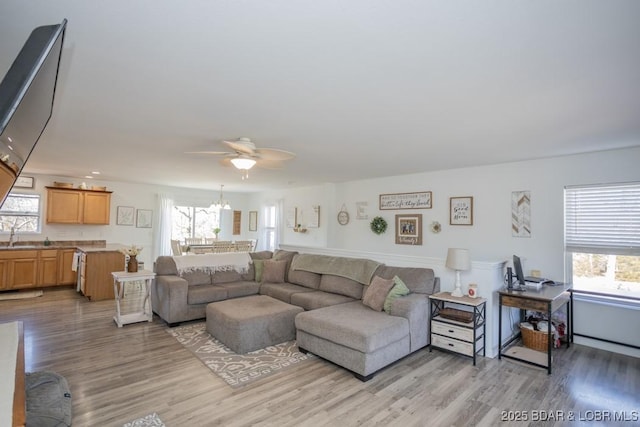 living room featuring sink, ceiling fan with notable chandelier, and light hardwood / wood-style flooring