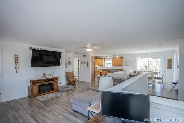 living room with ceiling fan with notable chandelier, sink, and light hardwood / wood-style floors