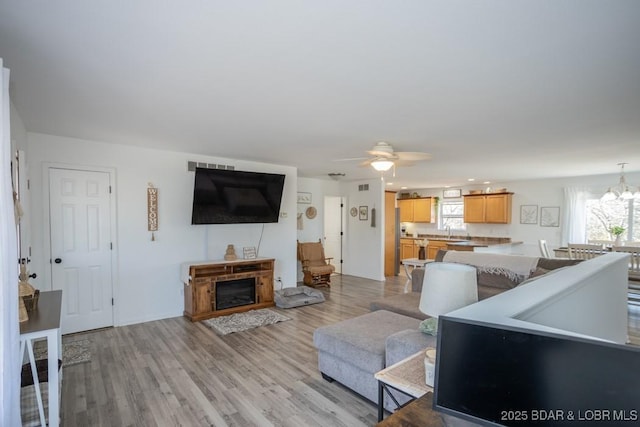 living room with plenty of natural light, sink, ceiling fan with notable chandelier, and light hardwood / wood-style flooring