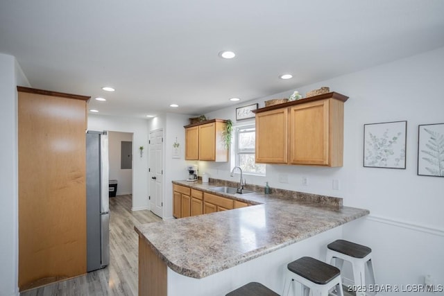 kitchen with a breakfast bar, sink, stainless steel fridge, light hardwood / wood-style floors, and kitchen peninsula