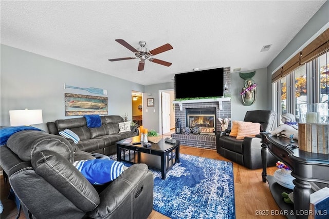 living room featuring ceiling fan, hardwood / wood-style floors, a brick fireplace, and a textured ceiling