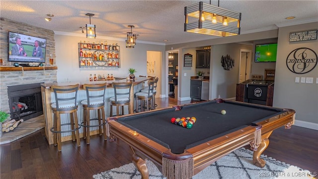 playroom with a large fireplace, crown molding, dark wood-type flooring, bar area, and a textured ceiling