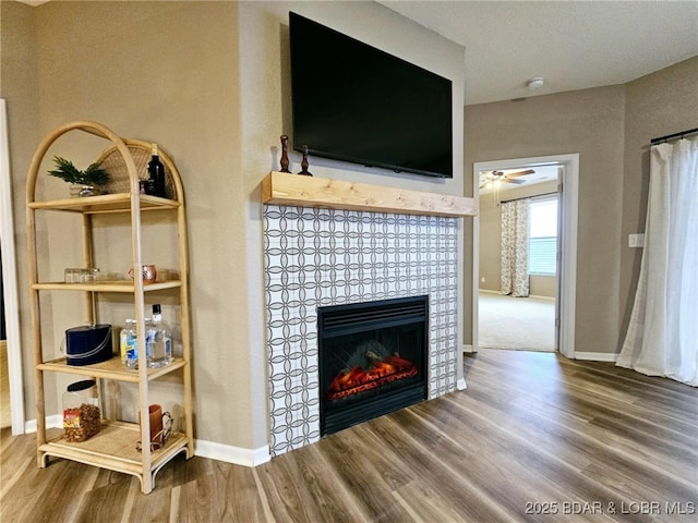 living area featuring baseboards, ceiling fan, a tiled fireplace, and wood finished floors