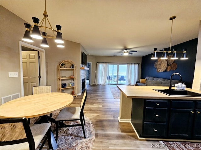 interior space with ceiling fan with notable chandelier, pendant lighting, sink, hardwood / wood-style flooring, and a center island with sink