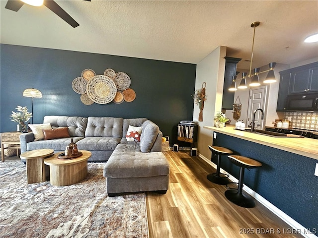 living room with hardwood / wood-style floors, a textured ceiling, sink, and ceiling fan