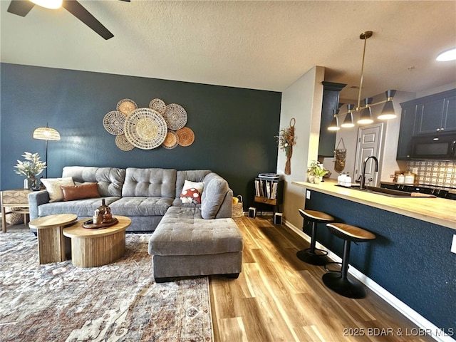 living room with baseboards, a textured ceiling, ceiling fan, and wood finished floors