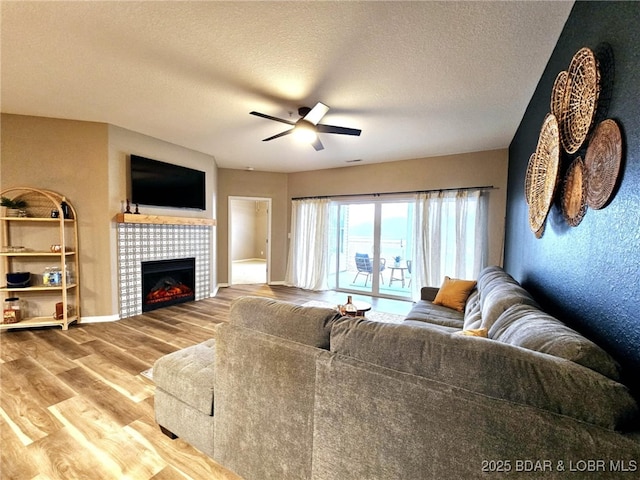 living room featuring hardwood / wood-style flooring, ceiling fan, a fireplace, and a textured ceiling