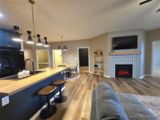 living room featuring baseboards, ceiling fan with notable chandelier, wood finished floors, and a tiled fireplace