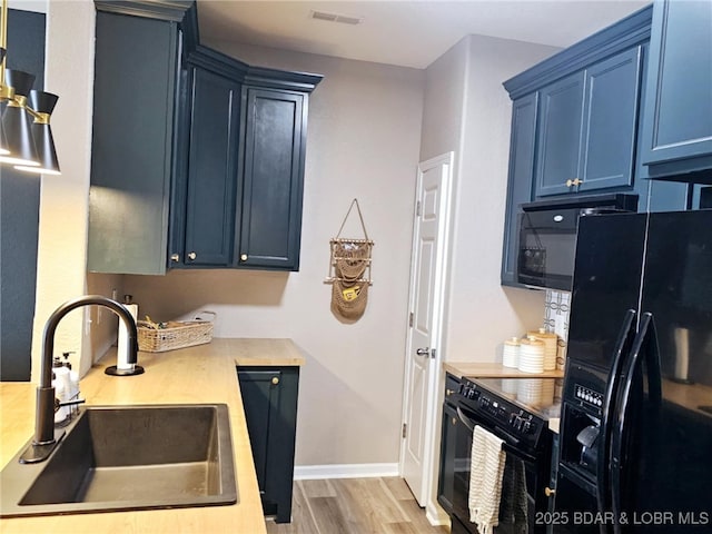 kitchen with blue cabinetry, butcher block countertops, sink, light hardwood / wood-style flooring, and black appliances